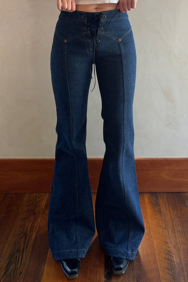 Person wearing blue flared jeans and a white top against a plain wall.